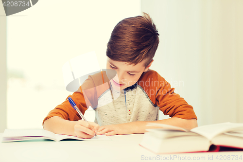 Image of smiling student boy writing to notebook at home