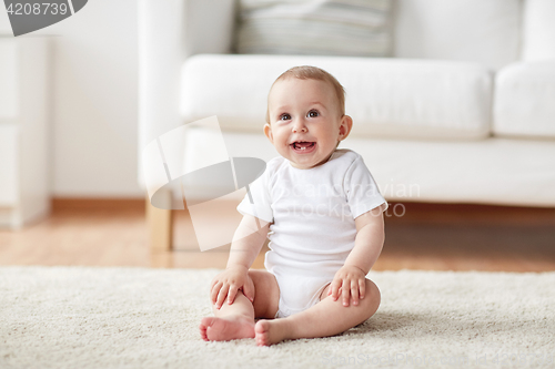 Image of happy baby boy or girl sitting on floor at home
