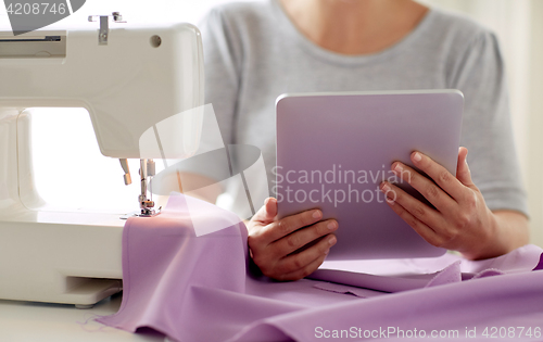 Image of tailor with sewing machine, tablet pc and fabric