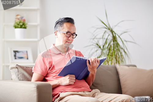 Image of man sitting on sofa and reading book at home