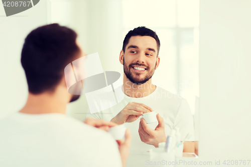 Image of happy young man applying cream to face at bathroom