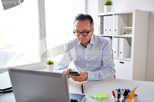 Image of businessman with laptop texting on smartphone