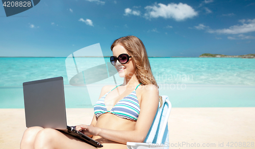 Image of woman with laptop sunbathing in lounge on beach