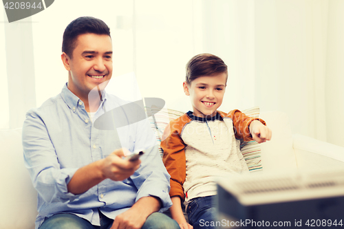 Image of smiling father and son watching tv at home