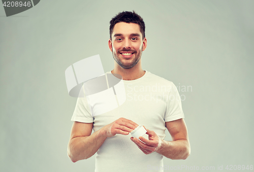 Image of happy young man with cream jar over gray