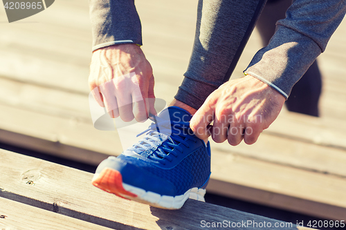 Image of close up of sporty man tying shoe laces outdoors