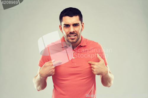 Image of angry man pointing finger to himself over gray