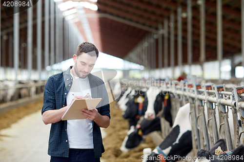 Image of farmer with clipboard and cows in cowshed on farm