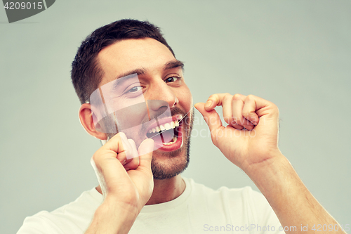 Image of man with dental floss cleaning teeth over gray
