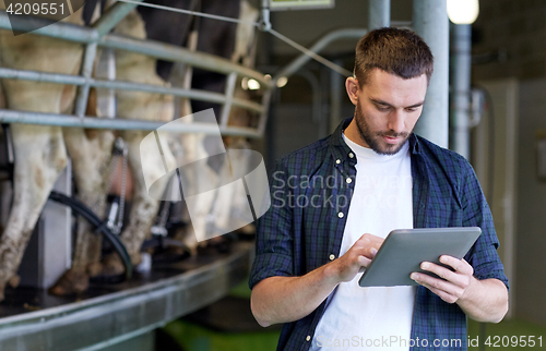 Image of young man with tablet pc and cows on dairy farm