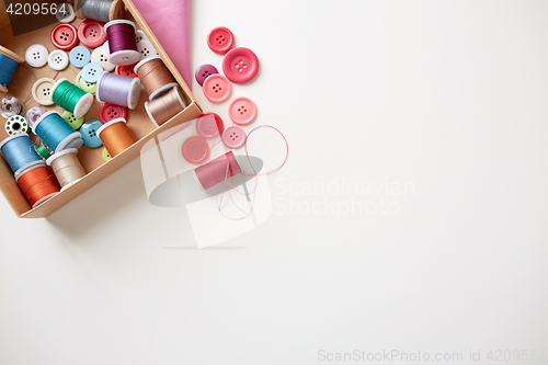 Image of box with thread spools and sewing buttons on table