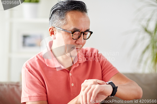 Image of asian man checking time on wristwatch at home