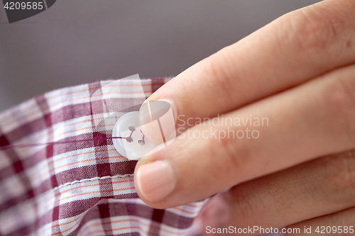 Image of woman with needle stitching on button to shirt