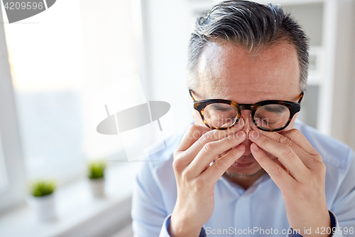 Image of businessman in glasses rubbing eyes at office