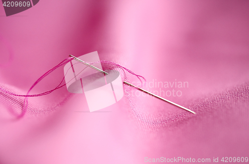 Image of sewing needle with thread stuck into pink fabric