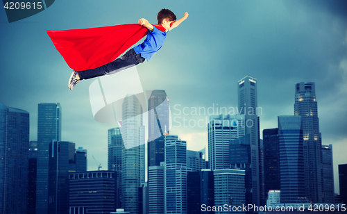 Image of boy in red superhero cape flying over city