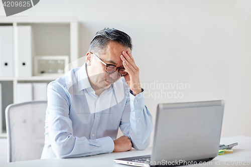 Image of businessman in eyeglasses with laptop at office
