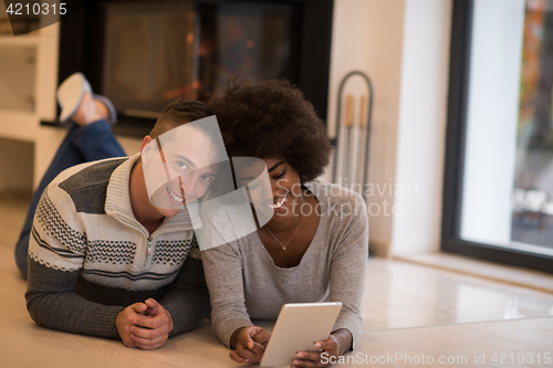 Image of multiethnic couple using tablet computer on the floor