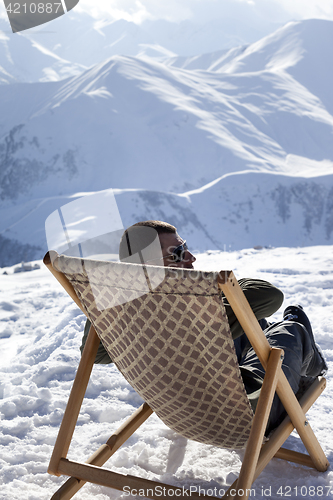 Image of Skier at winter mountains resting on sun-lounger at nice sun day