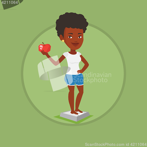 Image of Woman standing on scale and holding apple in hand.