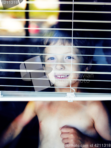 Image of Little cute boy throught window making funny faces, home alone l