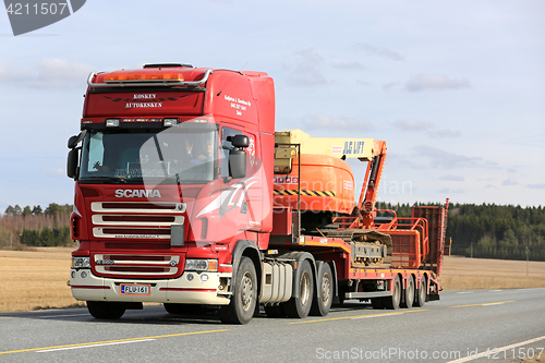 Image of Red Scania Semi Transports Boom Lift along Highway 