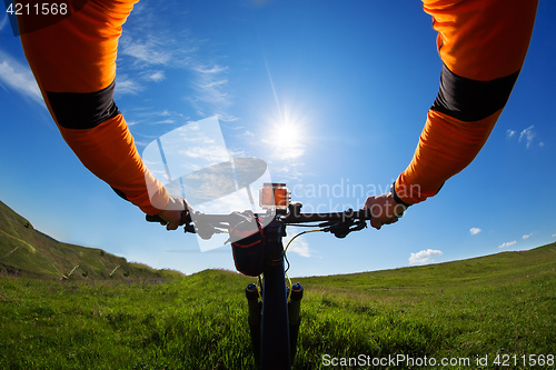 Image of Hands in orange jacket holding handlebar of a bicycle