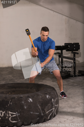 Image of man workout with hammer and tractor tire