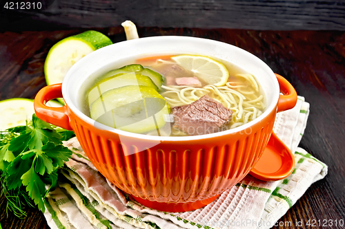 Image of Soup with zucchini and noodles in red bowl on kitchen towel