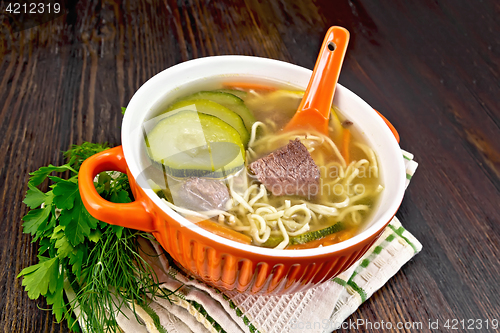 Image of Soup with zucchini and noodles in red bowl on napkin