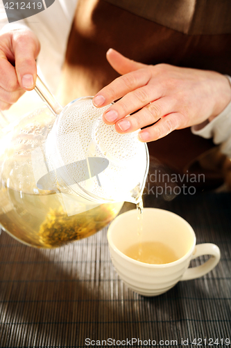 Image of Blooming tea brewed in a glass jug. Blooming tea. The waitress pours tea into a cup