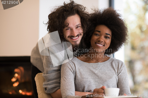 Image of multiethnic couple hugging in front of fireplace