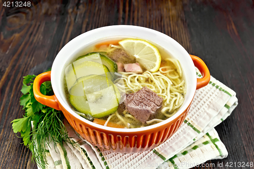 Image of Soup with zucchini and noodles in red bowl on wooden board