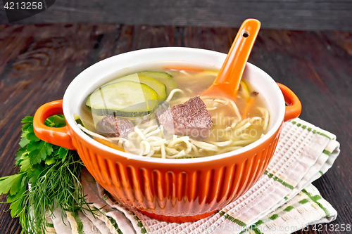 Image of Soup with zucchini and noodles in red bowl on dark board