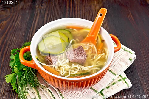 Image of Soup with zucchini and noodles in red bowl on board