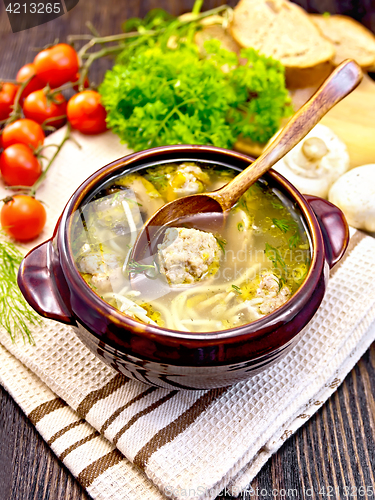 Image of Soup with meatballs and spoon in clay bowl on dark board