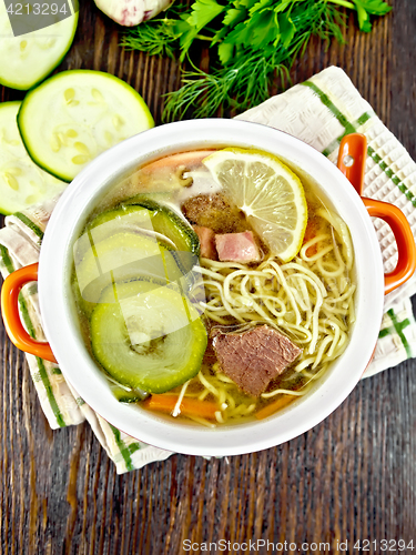 Image of Soup with zucchini and noodles in red bowl on board top