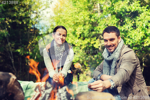 Image of happy couple roasting marshmallow over camp fire