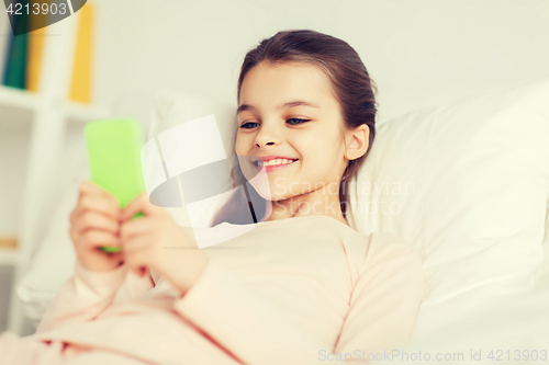 Image of happy girl lying in bed with smartphone at home