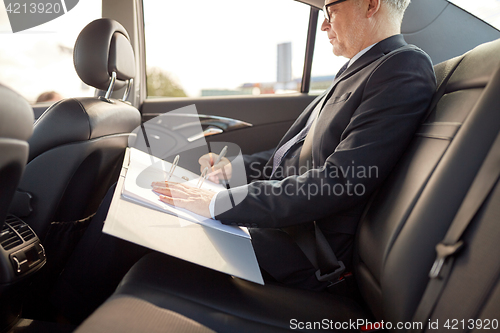 Image of senior businessman with papers driving in car