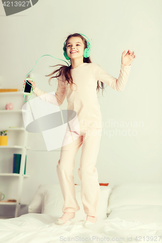 Image of girl jumping on bed with smartphone and headphones