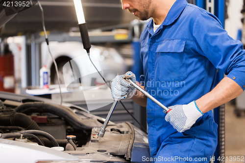 Image of mechanic man with wrench repairing car at workshop