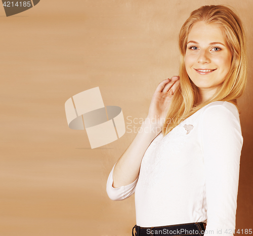 Image of young cool blong teenage girl messed with her hair smiling on warm brown background, lifestyle people concept