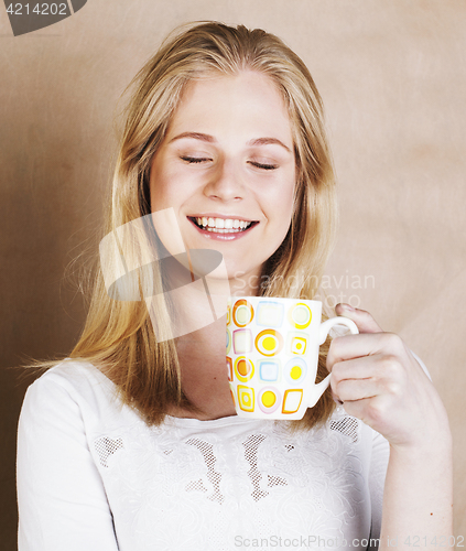 Image of young cute blond girl drinking coffee close up on warm brown bac