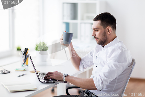Image of businessman with coffee typing on laptop at office