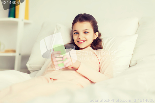 Image of happy girl lying in bed with smartphone at home