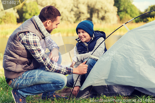 Image of happy father and son setting up tent outdoors