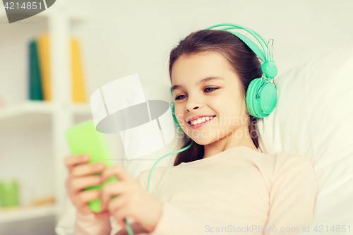 Image of happy girl lying in bed with smartphone at home