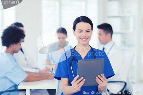 Image of happy doctor with tablet pc over team at clinic