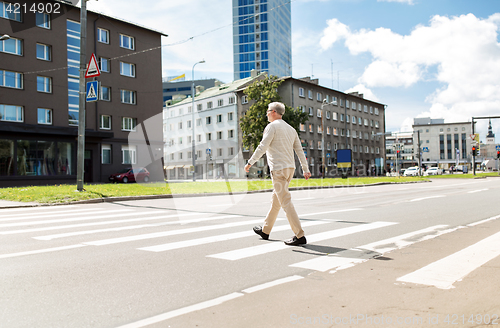 Image of senior man walking along city crosswalk